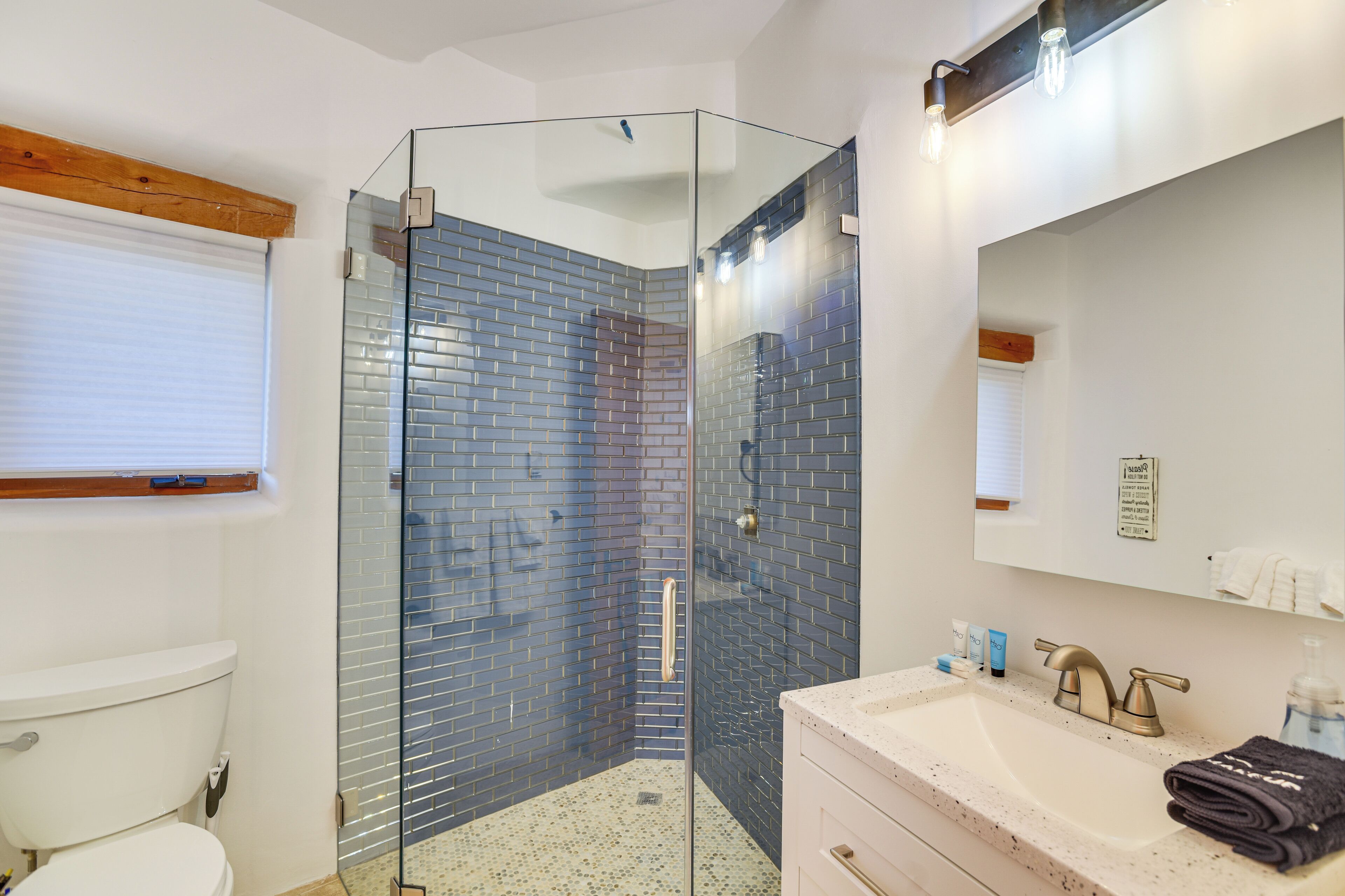 A modern bathroom with a glass-enclosed shower, a white sink with a gold faucet, and a mirror above the sink.