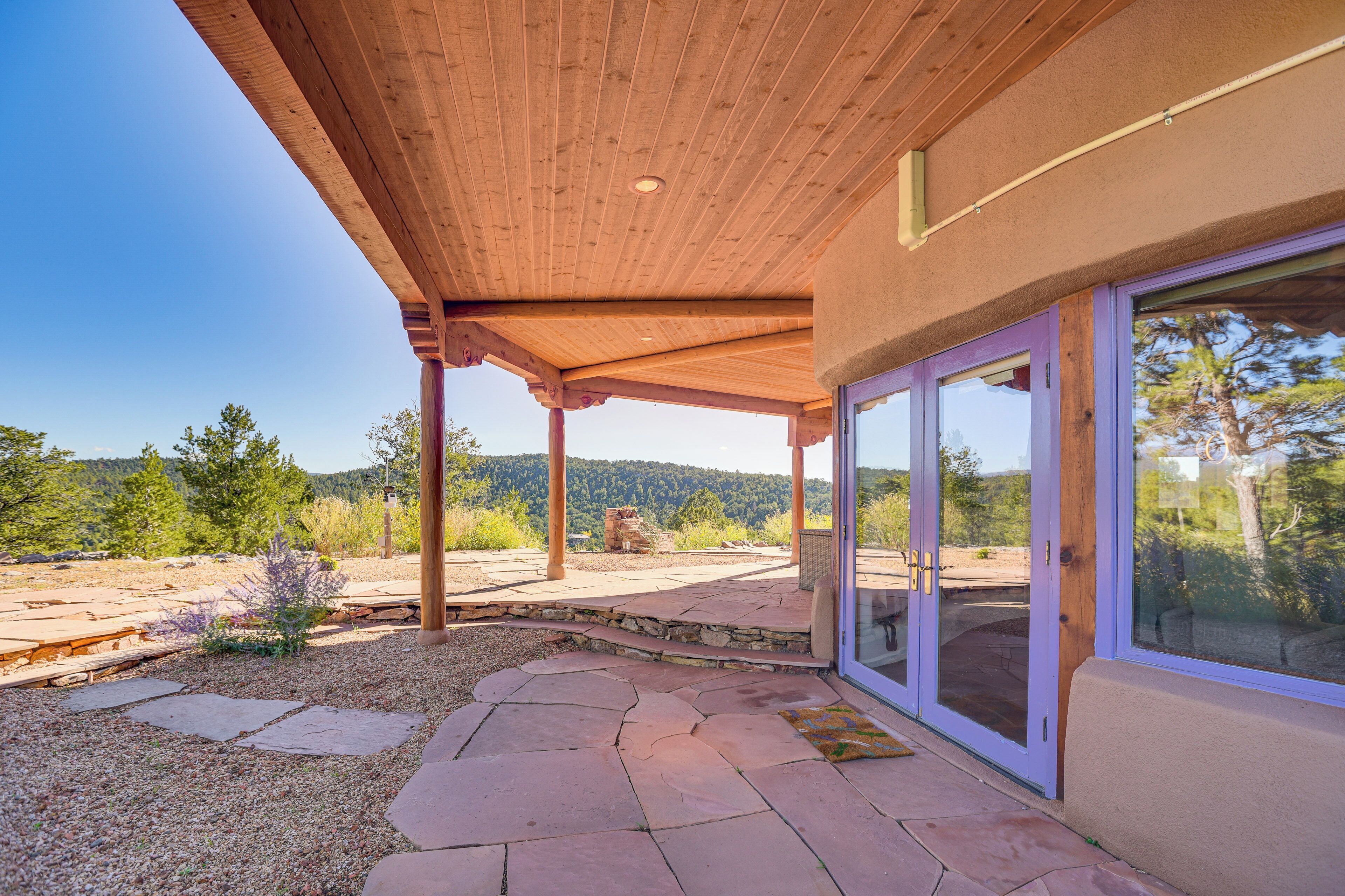 Un patio cubierto con suelo de piedra, vigas de madera y grandes puertas de cristal que dan a una zona exterior con vistas panorámicas.