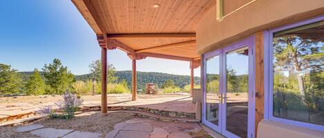 Un patio cubierto con suelo de piedra, vigas de madera y grandes puertas de cristal que dan a una zona exterior con vistas panorámicas.