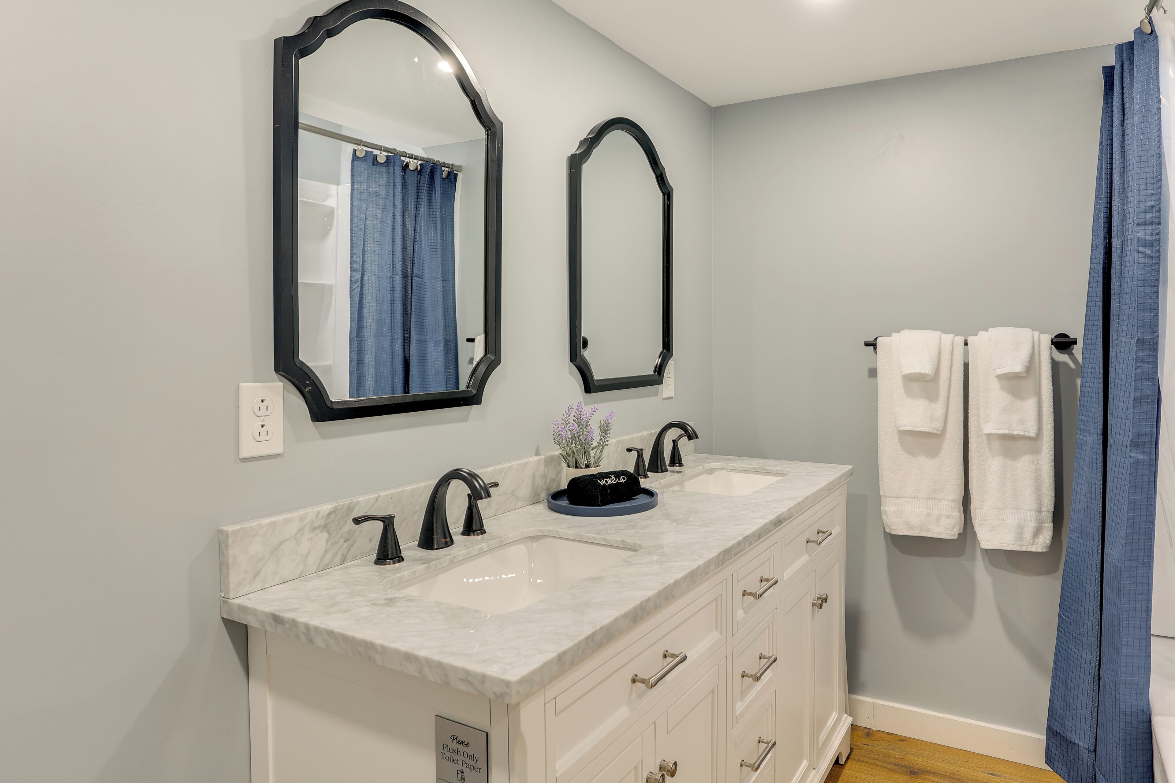 A bathroom with a double sink vanity, two mirrors, a towel rack with towels, and a shower curtain.