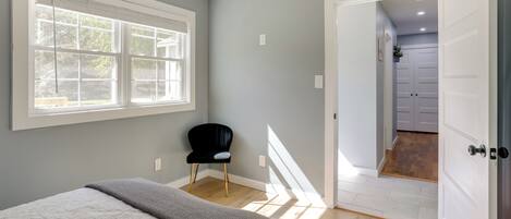 A bedroom with a large window, a black chair, and a bed with a grey blanket.