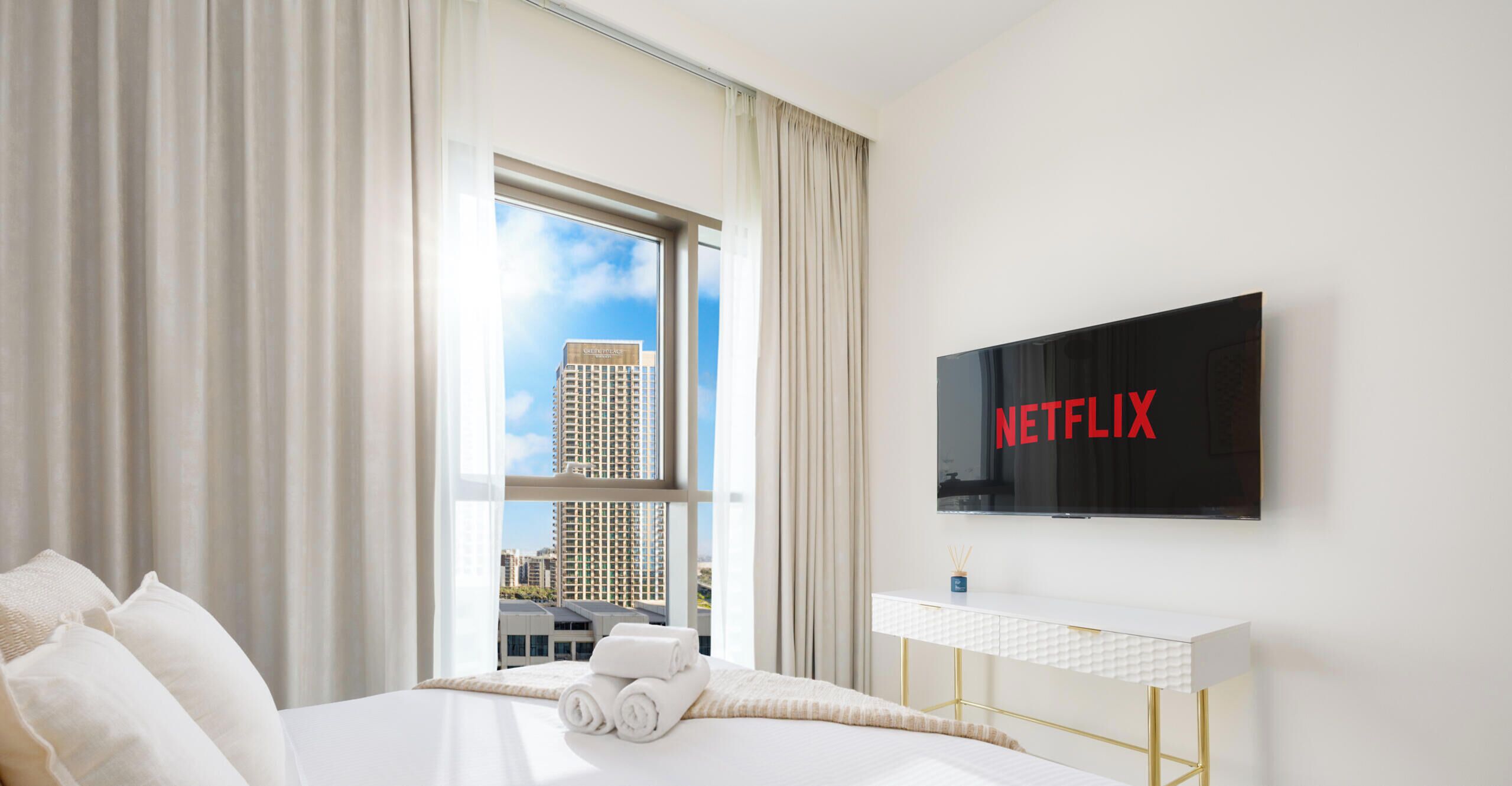 Een hotelkamer met een bed, een televisie, een bureau en een raam met uitzicht op gebouwen.