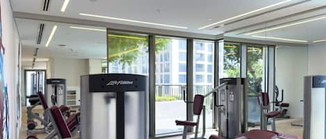 Une salle de sport moderne dotée de divers appareils d’entraînement, de grandes fenêtres et d’un aménagement propre et spacieux.