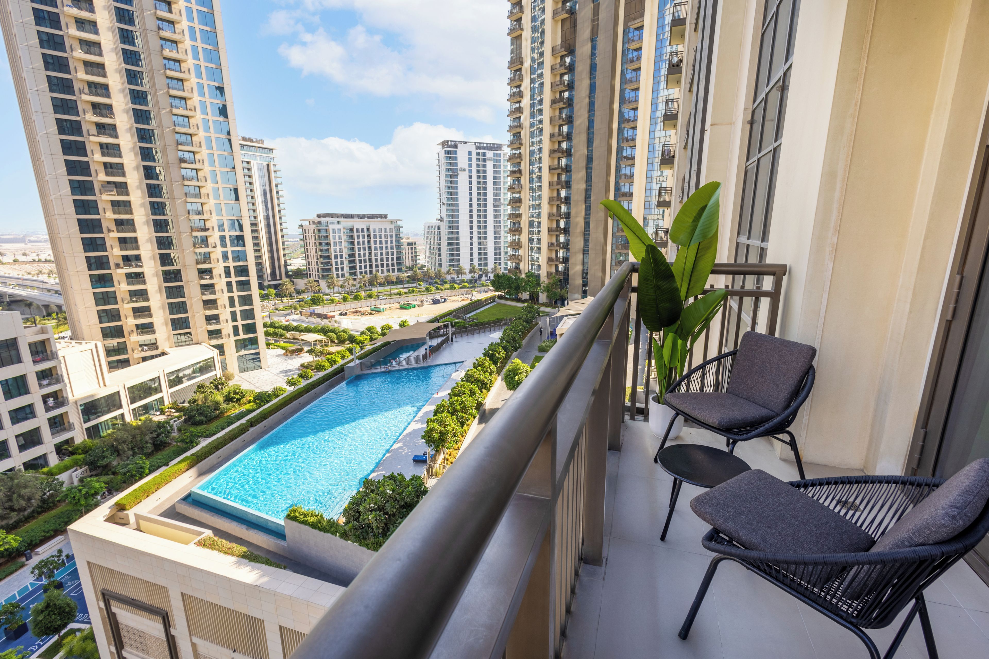 A balcony with a view of a swimming pool, high-rise buildings, and a clear sky.