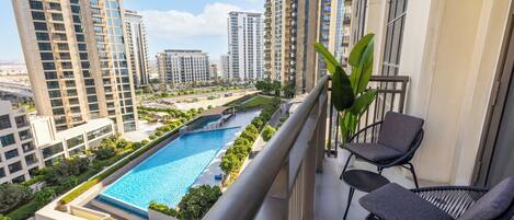 A balcony with a view of a swimming pool, high-rise buildings, and a clear sky.