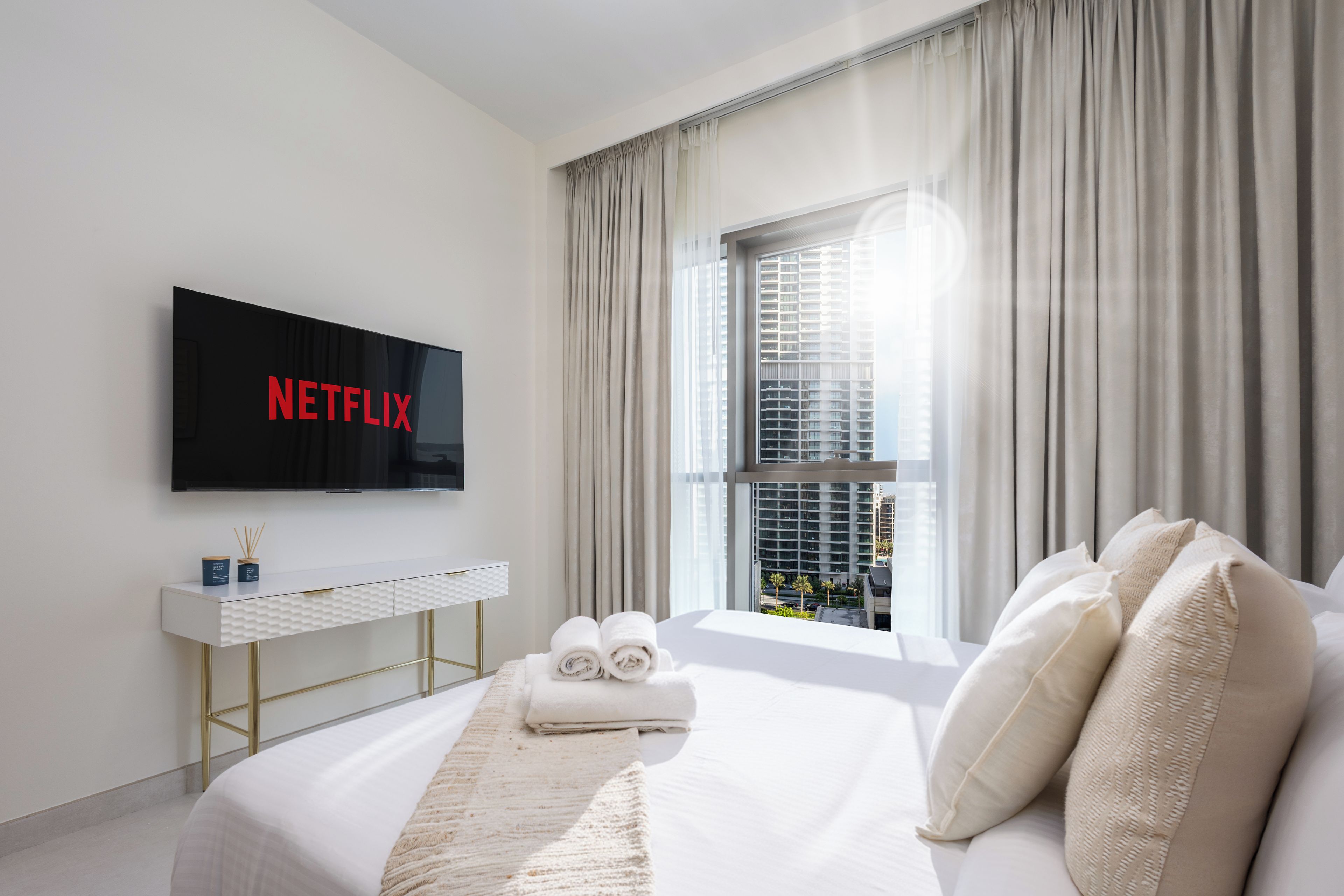Een moderne hotelkamer met een groot bed, een flatscreen televisie aan de muur, een witte console en een raam met gordijnen.