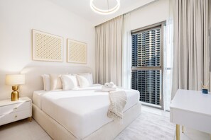 A modern hotel room with a large bed, a bedside table, a lamp, a desk, and a view of a high-rise building. - LUX  The Creekside Skyline View Suite (Dubai)
