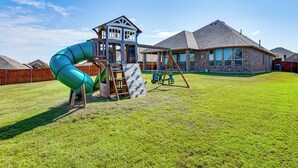 Une aire de jeux avec un toboggan et un mur d’escalade, entourée d’une cour verdoyante et d’un bâtiment doté d’un toit en pente.