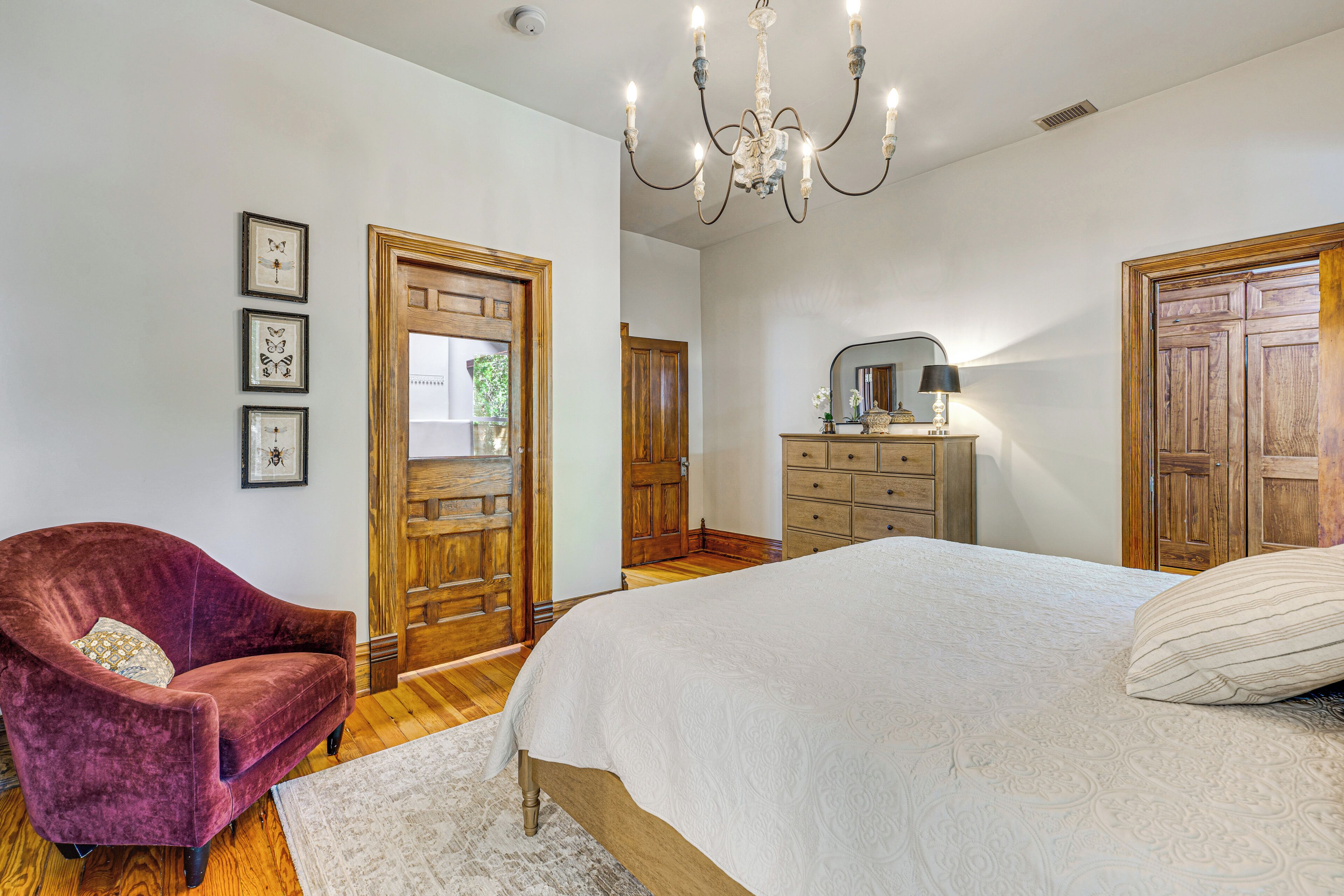 A bedroom with a large bed, a wooden wardrobe, a dresser, a chair, and a chandelier.