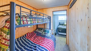 Une chambre avec un lit superposé, un intérieur en bois, un luminaire au plafond et une porte donnant sur une autre pièce.