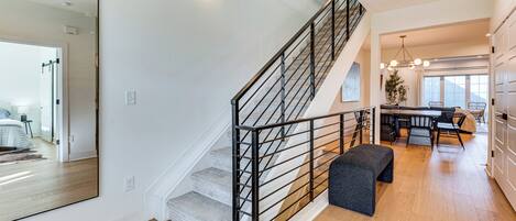 A modern interior with a staircase, a dining area, and a large mirror reflecting a bedroom.