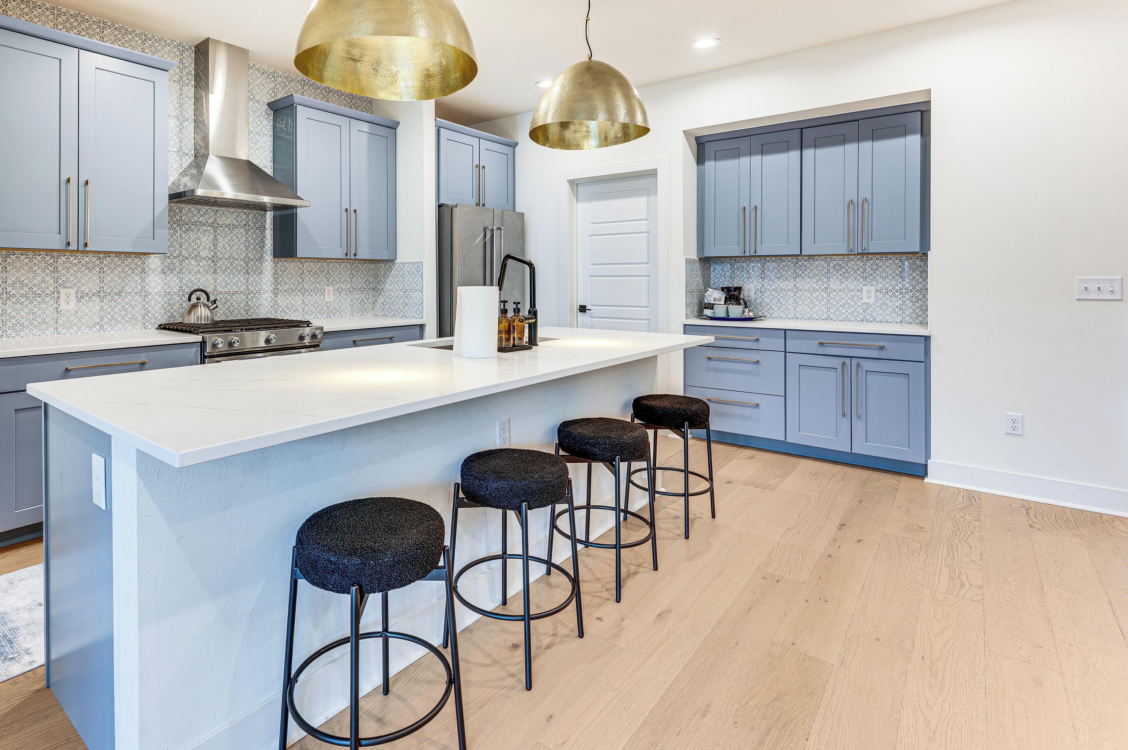 A modern kitchen with blue cabinets, a central island with stools, stainless steel appliances, and pendant lighting.