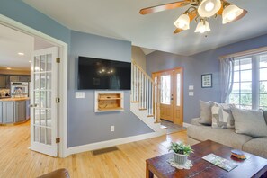 A spacious living room with a wooden floor, a large flat-screen TV mounted on the wall, a staircase leading to another level, and a cozy seating area with a sofa and a coffee table.