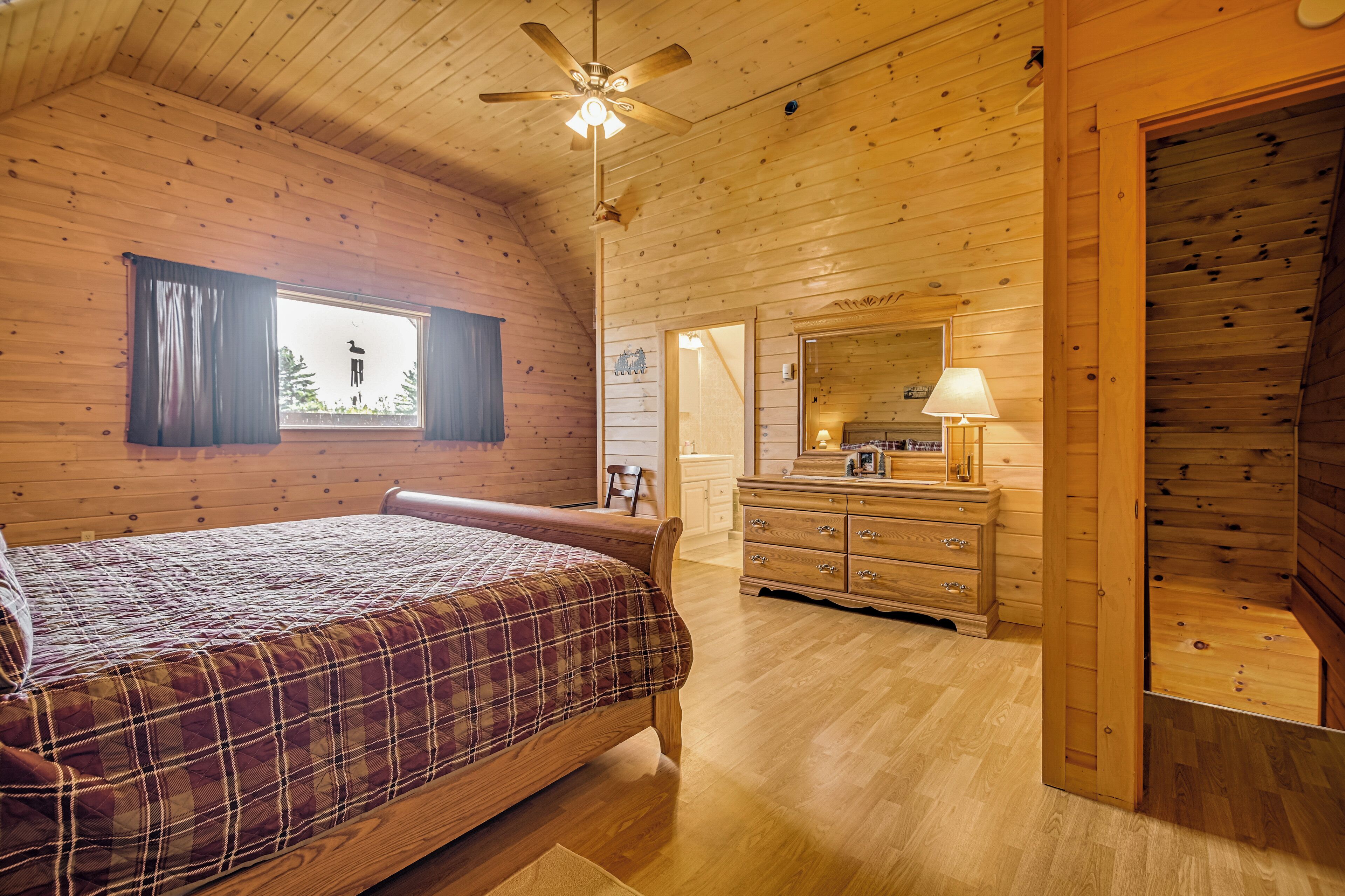 A wooden cabin bedroom with a bed, dresser, and ceiling fan.