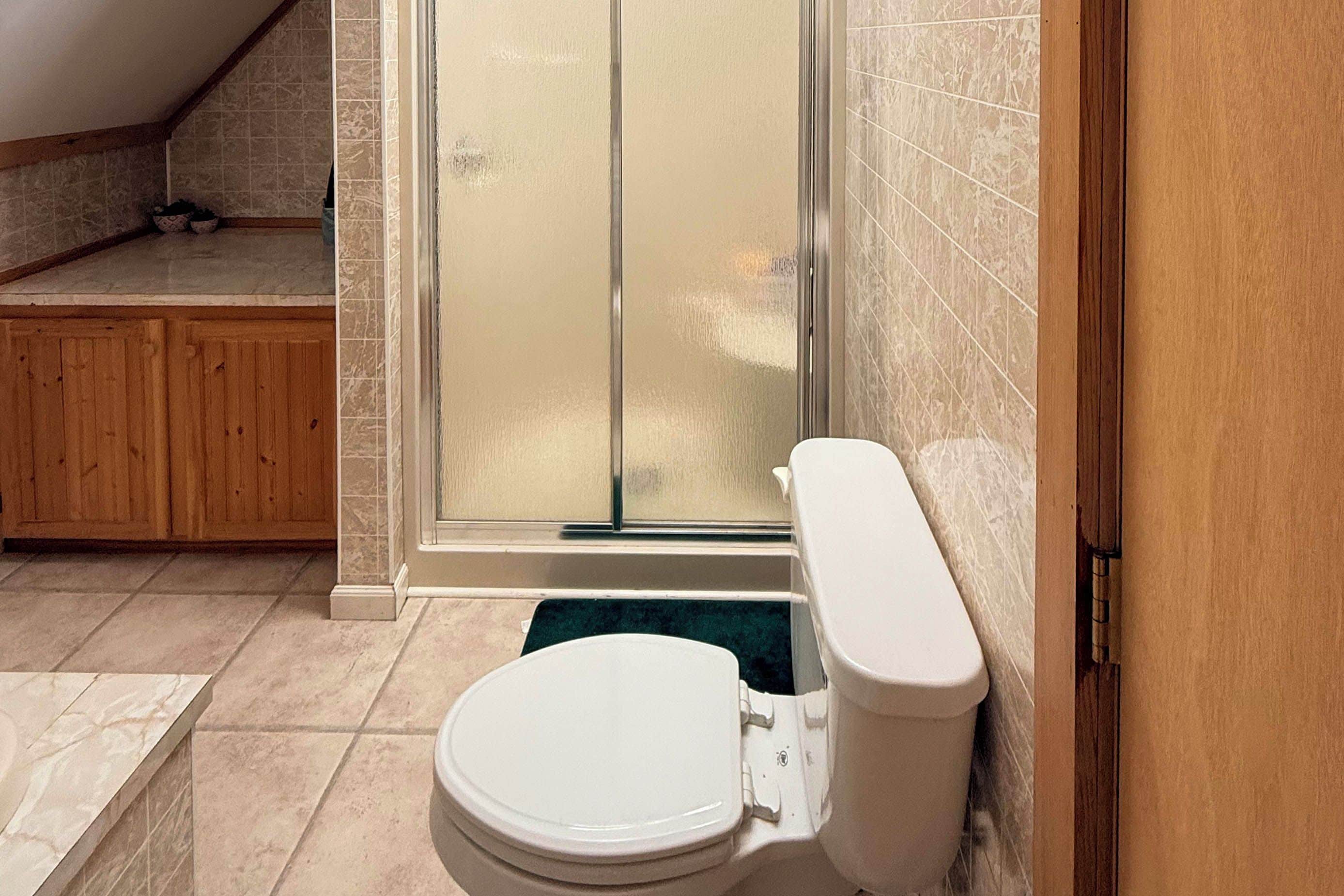 A bathroom with a toilet, a shower enclosure, and a wooden cabinet.