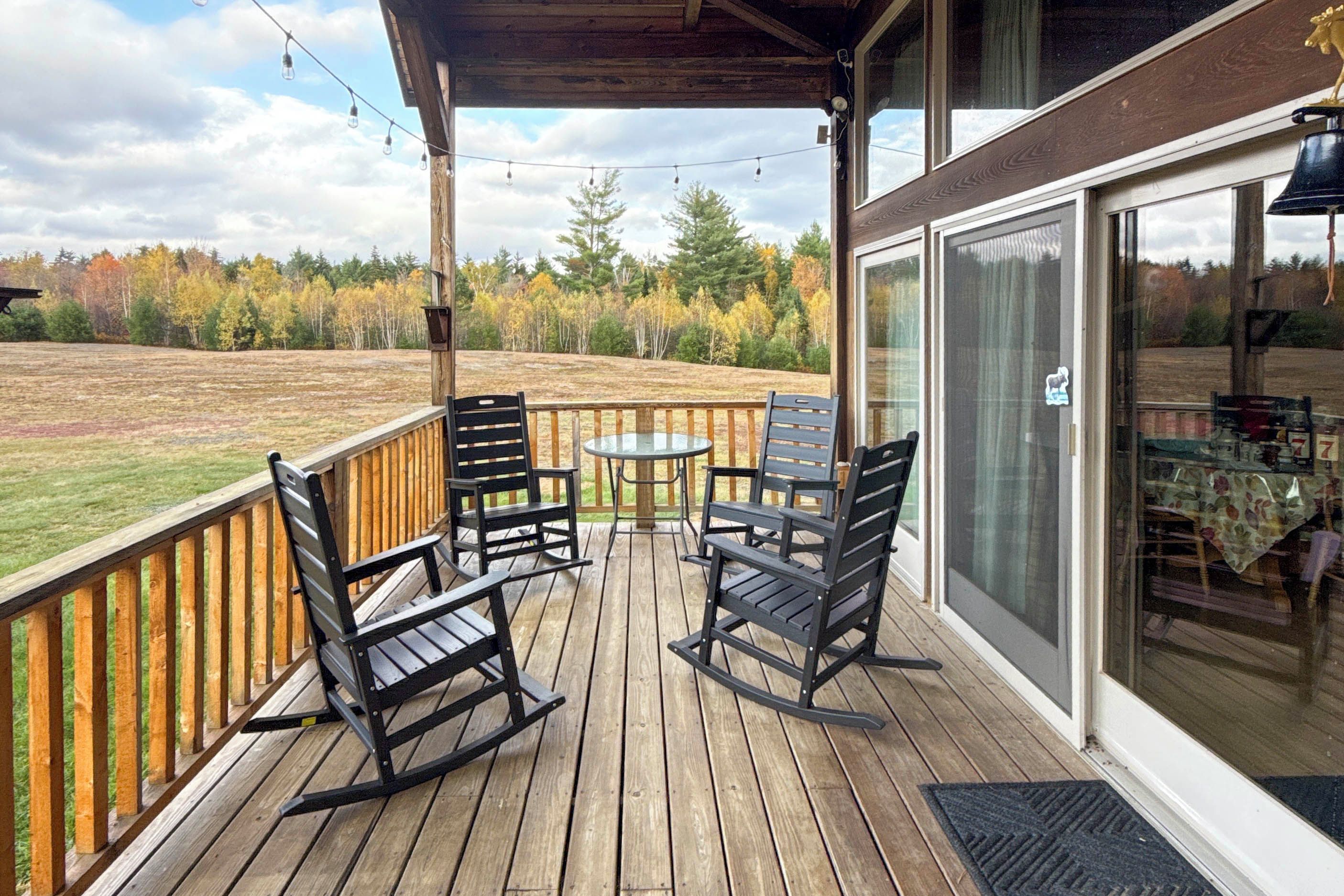 A wooden deck with outdoor furniture, a glass door, and a view of a forested area.