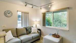 Un salon avec un canapé, une table d’appoint, une lampe, une horloge et une fenêtre avec des rideaux.