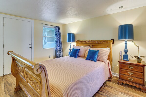 A bedroom with a wooden bed, two bedside tables with lamps, a window with curtains, and a door. - Industrial Grade Comfort: Near Ports & Plants (Port Arthur)