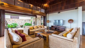A spacious living area with a stone wall, a large sofa set, a coffee table, a television, and a stone fireplace. - Ban Kinaree (Koh Samui)