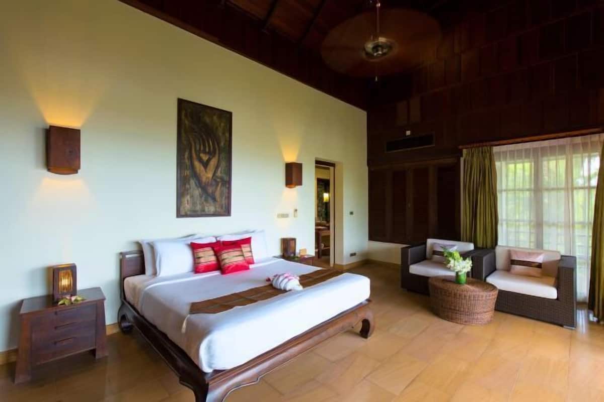 A spacious bedroom with a large bed, a wooden ceiling, and a view of the outdoors through a window.