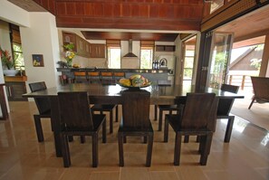 A spacious dining area with a large island, dark wooden chairs, and a tiled floor. - Ban Kinaree (Koh Samui)