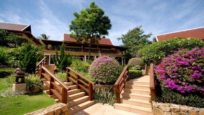 A building with a staircase leading to a covered entrance, surrounded by lush greenery and flowering plants. - Ban Kinaree (Koh Samui)