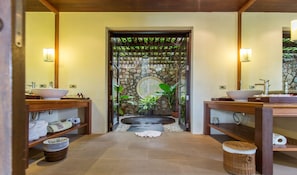 A bathroom with two sinks, a stone wall, a circular window, and a small waterfall feature. - Ban Kinaree (Koh Samui)