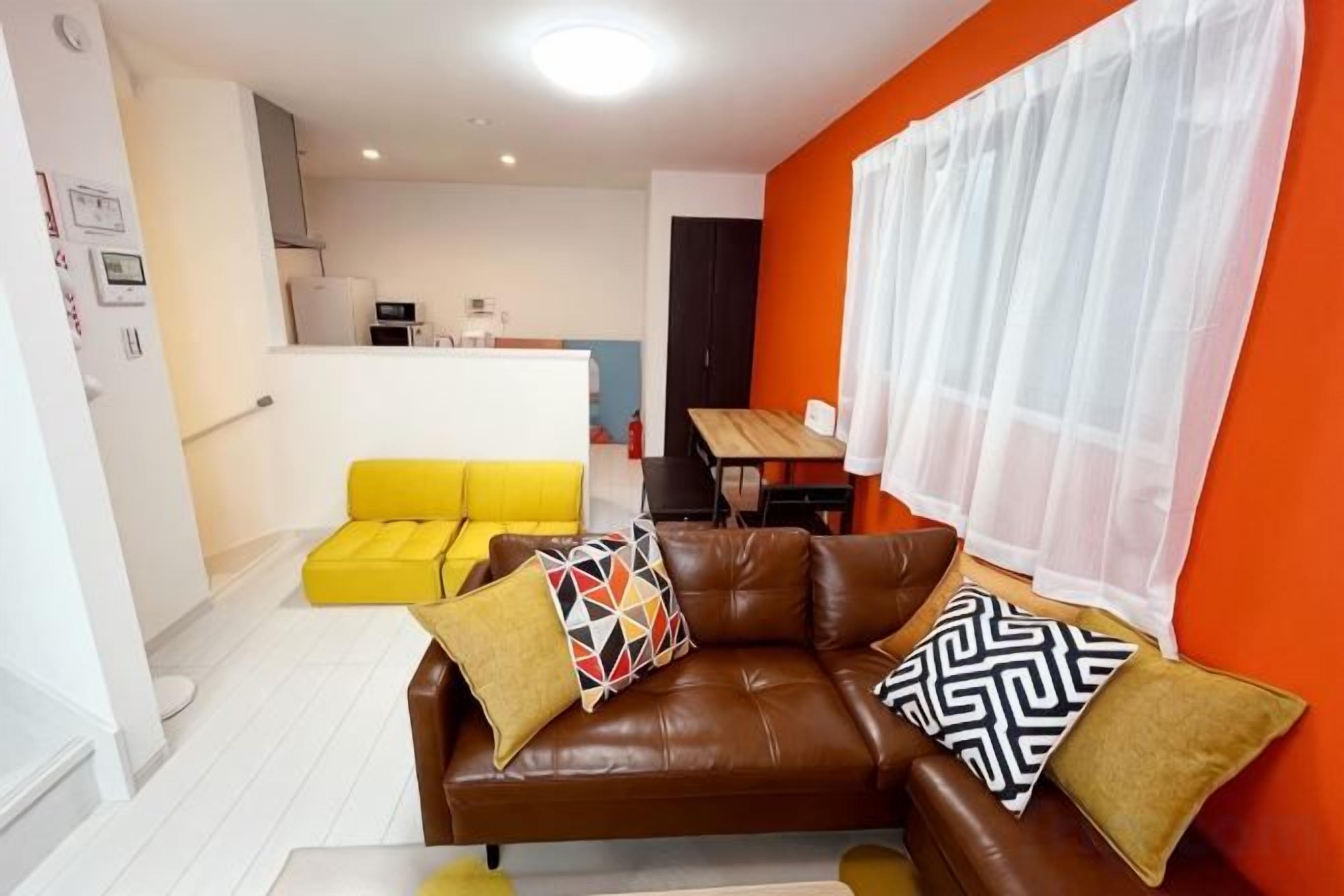 A living room with a brown leather sofa, yellow sofa, and a dining table.