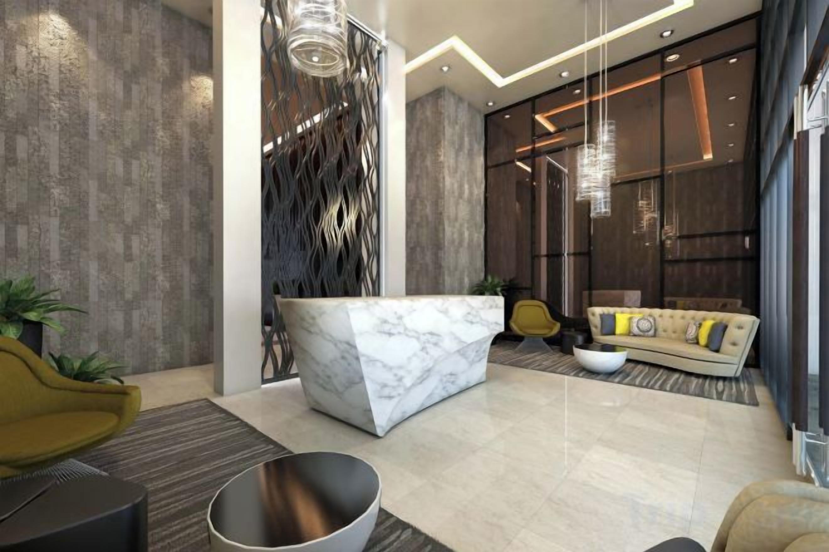 A modern lobby with a marble reception desk, a sofa with cushions, a yellow chair, and a large window.