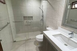 A bathroom with a glass-enclosed shower, a toilet, and a sink with a mirror above it. - WS Hotel (Taguig)