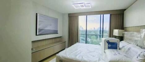 Habitación de hotel con cama, televisor, ventana con vista a la ciudad y mesita de noche con lámpara.