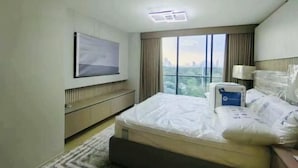 Ett hotellrum med en säng, ett sängbord, en lampa, en tv som är monterad på väggen och ett fönster med utsikt över staden.
