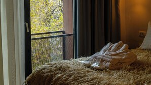 A hotel room with a bed, a window with curtains, a wall-mounted light fixture, and a view of trees outside. - NISHANI BOUTIQUE MOTEL (Bucharest)