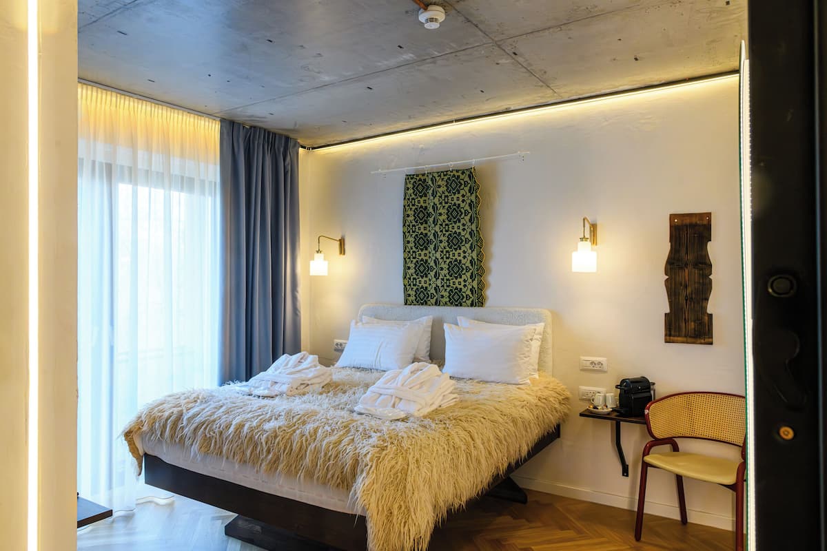 A modern hotel room with a large bed, a chair, and a wall-mounted light fixture.