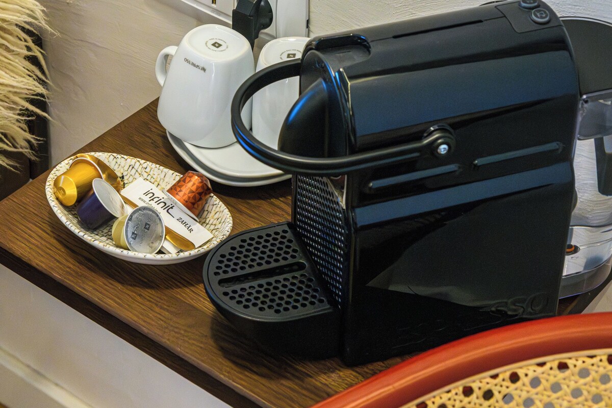 A coffee maker on a table with a power outlet, a cup, and a plate with a cup and a small item.