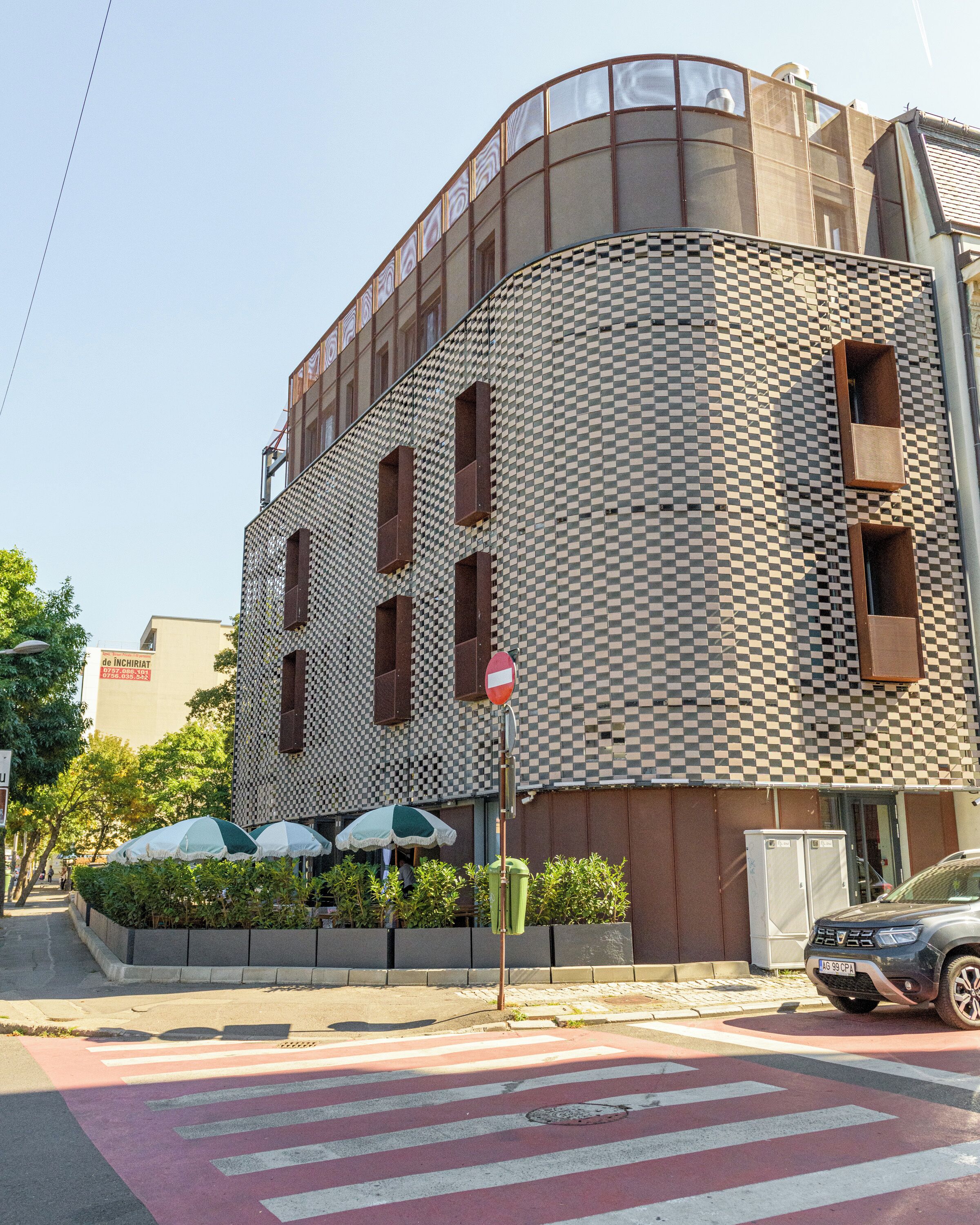 Un edificio con fachada a cuadros, una señal de prohibido el paso y un paso de peatones al frente.