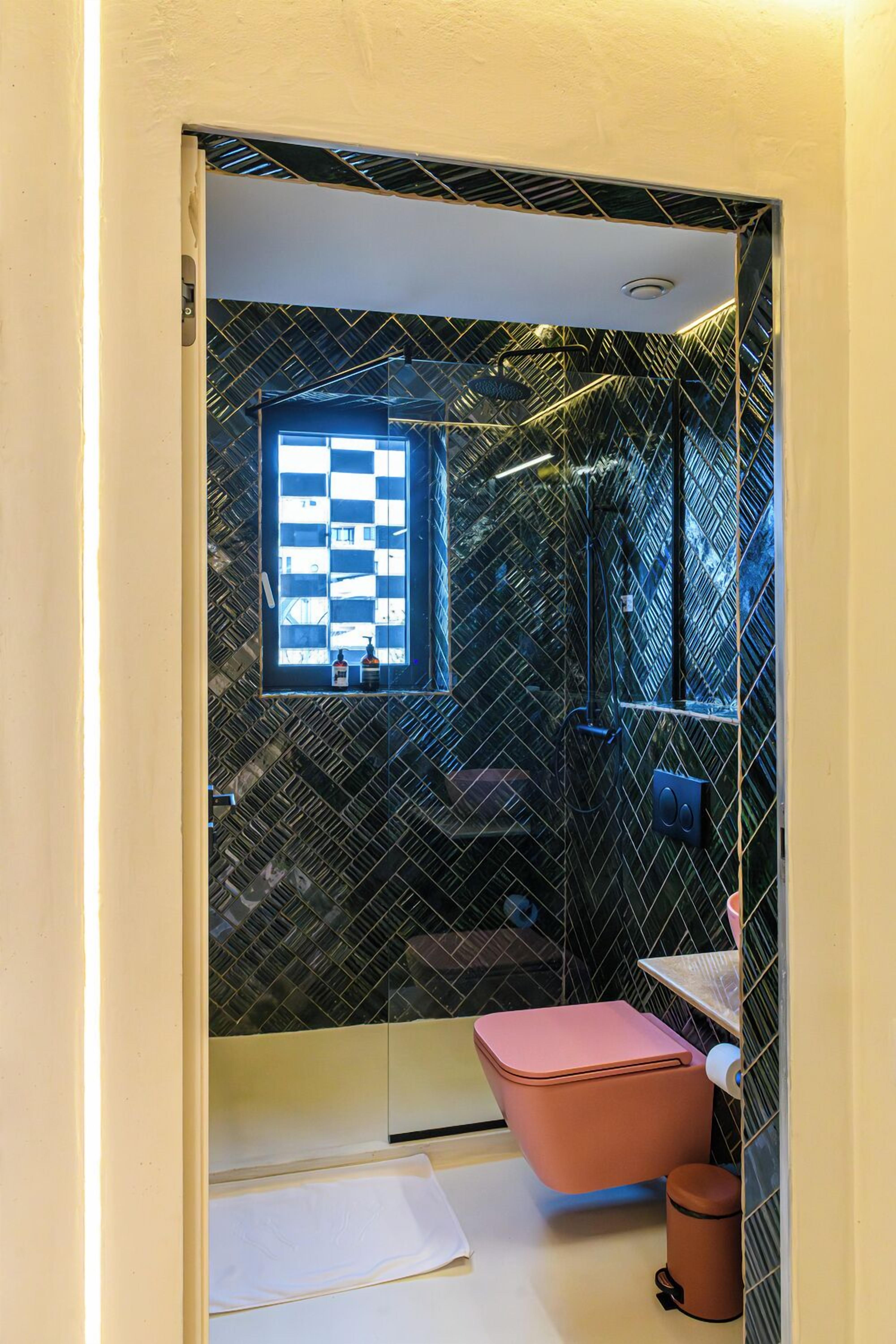 A bathroom with a checkered window, a pink toilet, and a shower area.
