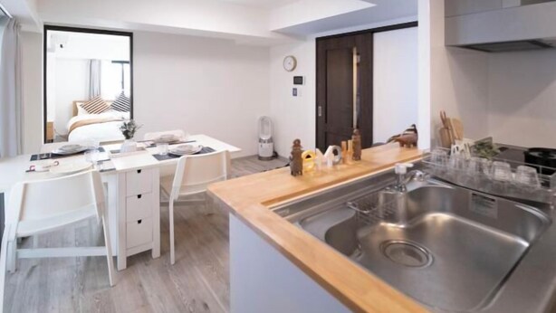 A modern kitchen with a wooden countertop, stainless steel sink, and white cabinetry. - The Peak Kuromon (Osaka)