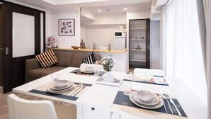 A modern dining area with a white table set for two, a grey sofa, and a kitchen area in the background. - The Peak Kuromon (Osaka)