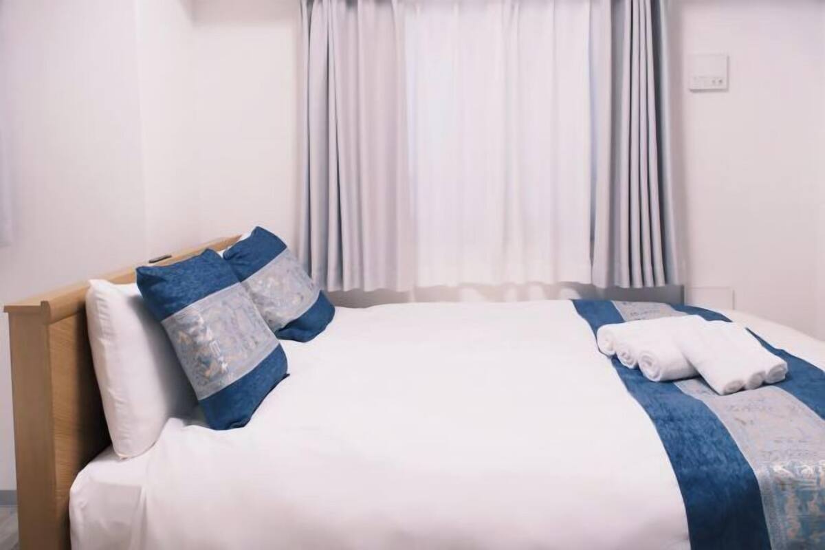 A neatly made bed with a blue and white bedspread, white pillows, and a rolled towel on the side.
