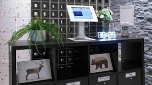 A reception desk with a digital screen, a clock, and a plant. There are labeled drawers below the desk. - The Peak Kuromon (Osaka)