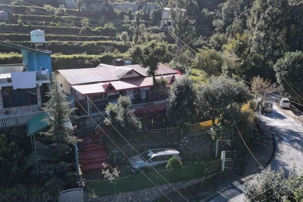 A house with a red roof, surrounded by greenery and a road.