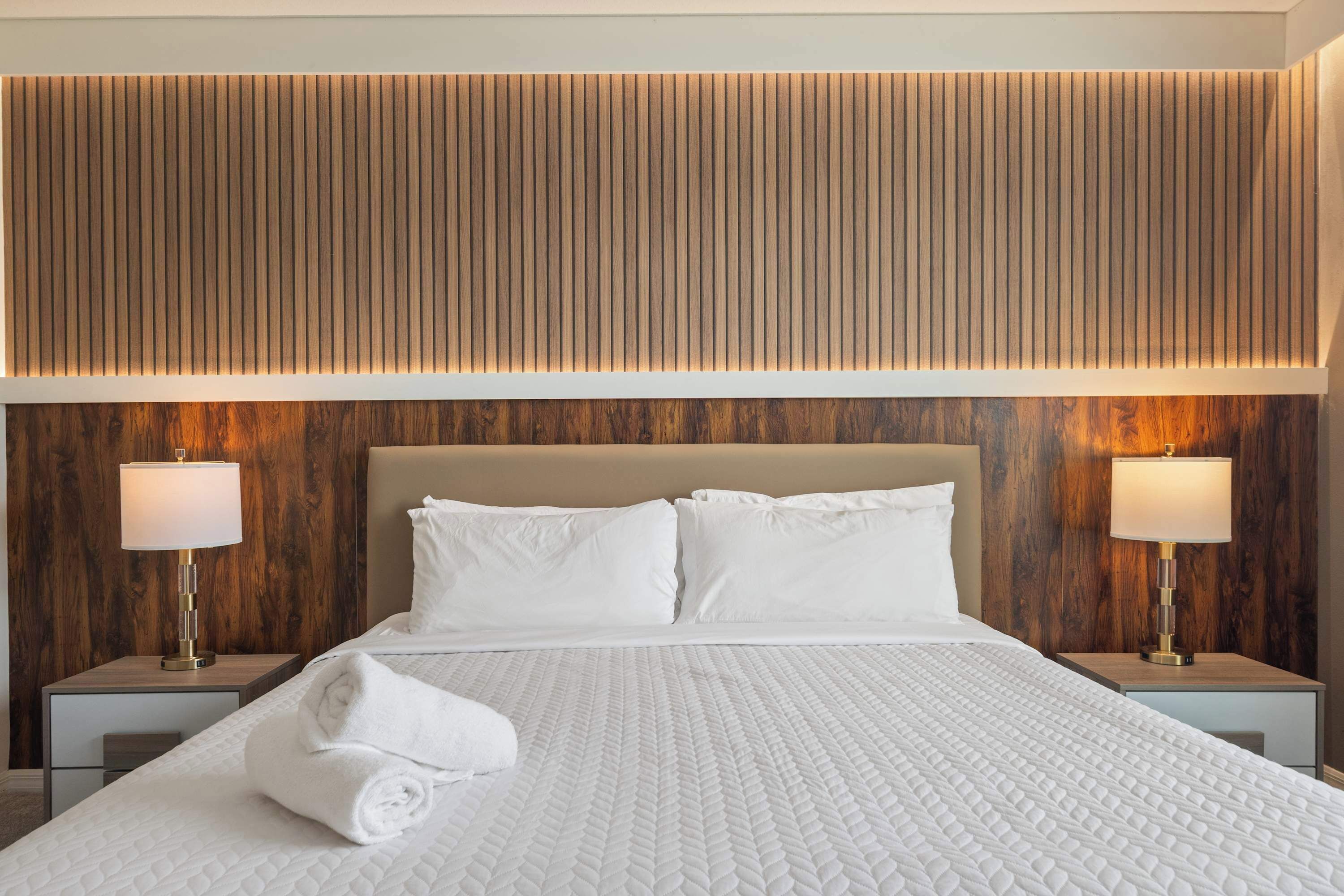 Ein Hotelzimmer mit einem großen Bett, zwei Nachttischen mit Lampen und einer Wandpaneele aus Holz.