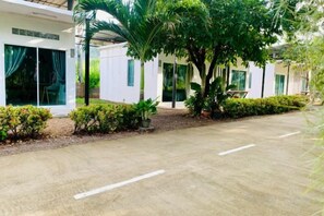 A paved driveway leading to a building with a covered outdoor seating area, surrounded by greenery and a palm tree. - Suan Lung Rin Resort Cha Am (Cha-am)