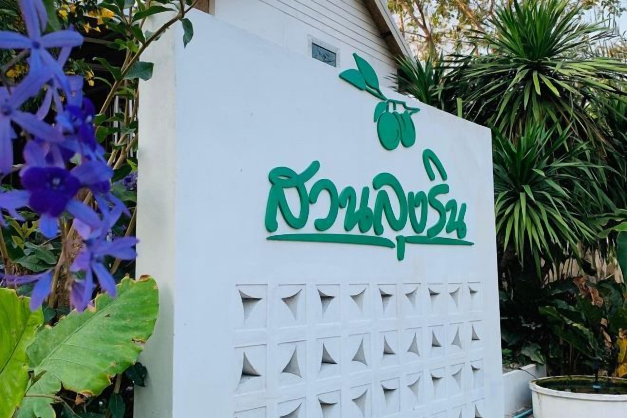 A white sign with green text and a leaf symbol, surrounded by greenery.