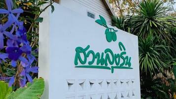 A white sign with green text and a leaf symbol, surrounded by greenery.
