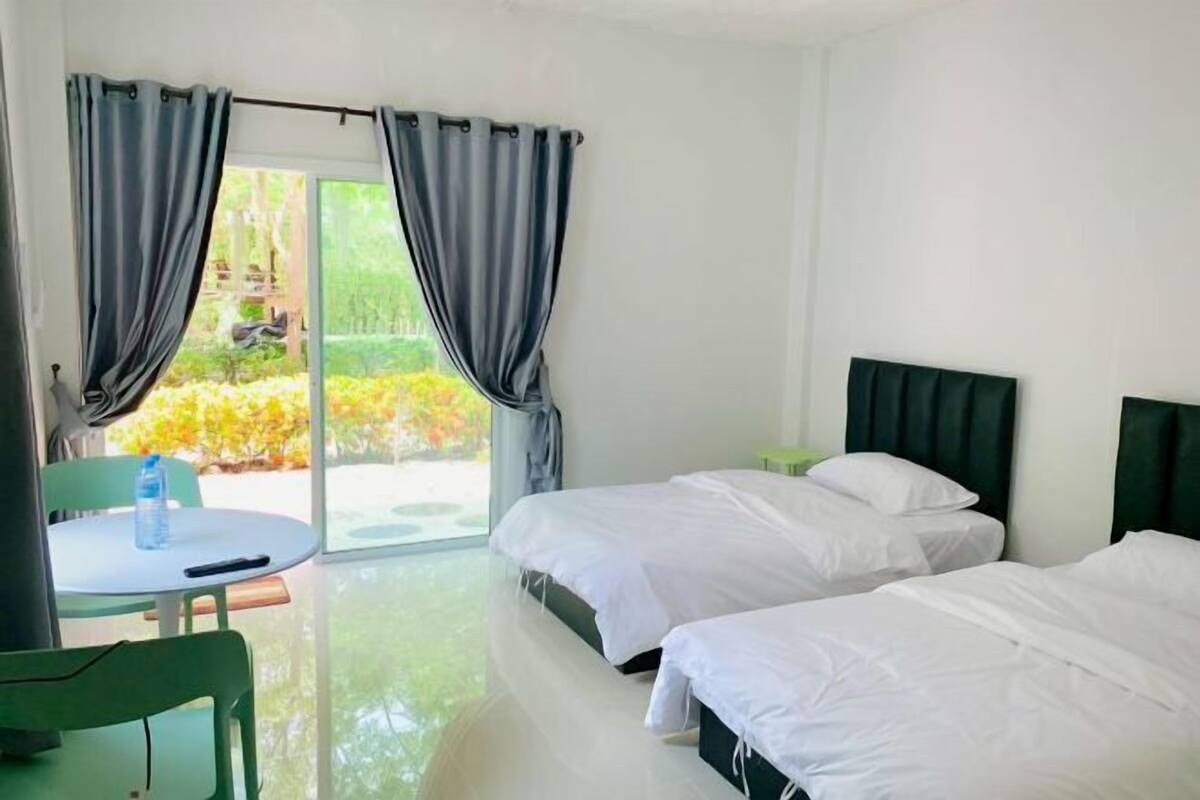 A hotel room with two beds, a small table with a chair, and a view through a glass door.