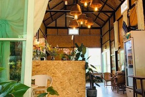 A rustic interior with a high ceiling, exposed beams, and a wooden partition. There are wicker chairs and a refrigerator. - Suan Lung Rin Resort Cha Am (Cha-am)