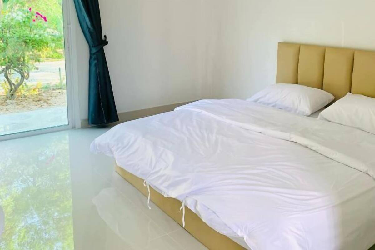 A bedroom with a bed, a window with curtains, and a view of greenery outside.