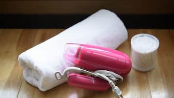 A white towel, a pink hairdryer, and a white container on a wooden surface.